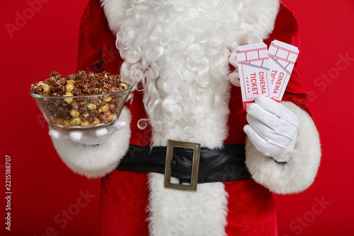Santa Claus with bowl of sweet popcorn  and cinema tickets on red background....