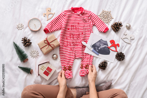 Young pregnant woman with pregnancy test, baby clothes, sonogram image and Ch...