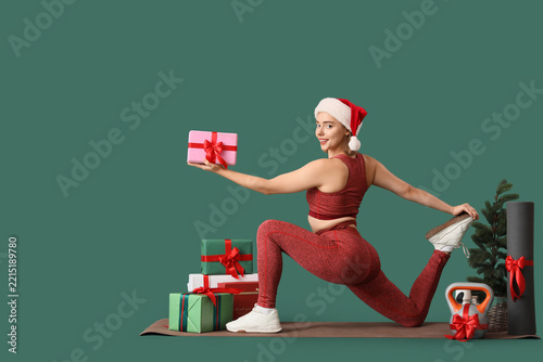 Sporty young woman with Christmas gift boxes, kettlebell and yoga mat exercis...