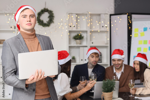 Young man with laptop celebrating New Year at corporate party in office