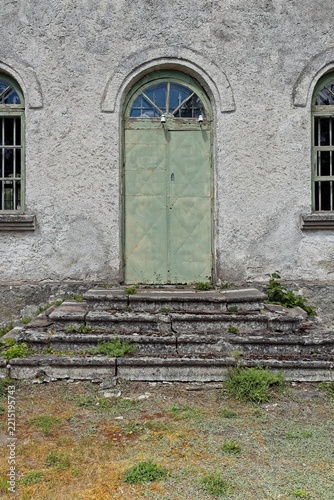 Arched doorway with a weathered green metal door set into a light-colored, textured plaster wall, Estonia, Europe.