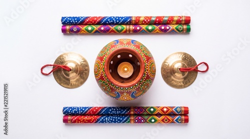Traditional Navratri dance kit flat lay with hand-painted terracotta Garba pot, lit diya, dandiya sticks and manjira cymbals
