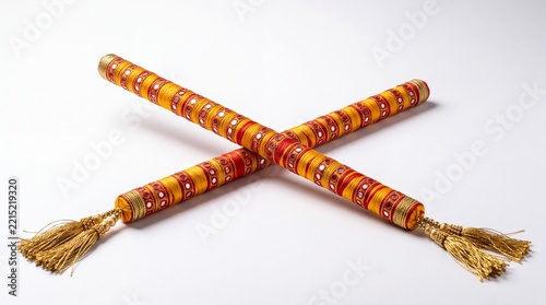 Gujarati dandiya sticks crossed on white surface, wrapped in saffron yellow and crimson red silk with embroidered mirrors