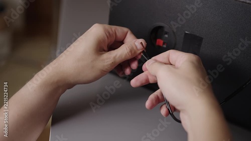 Close-up view of person hands preparing copper speaker wire by twisting strands, getting ready to connect it to terminals on back of audio system, closeup, cropped shot, slow motion.