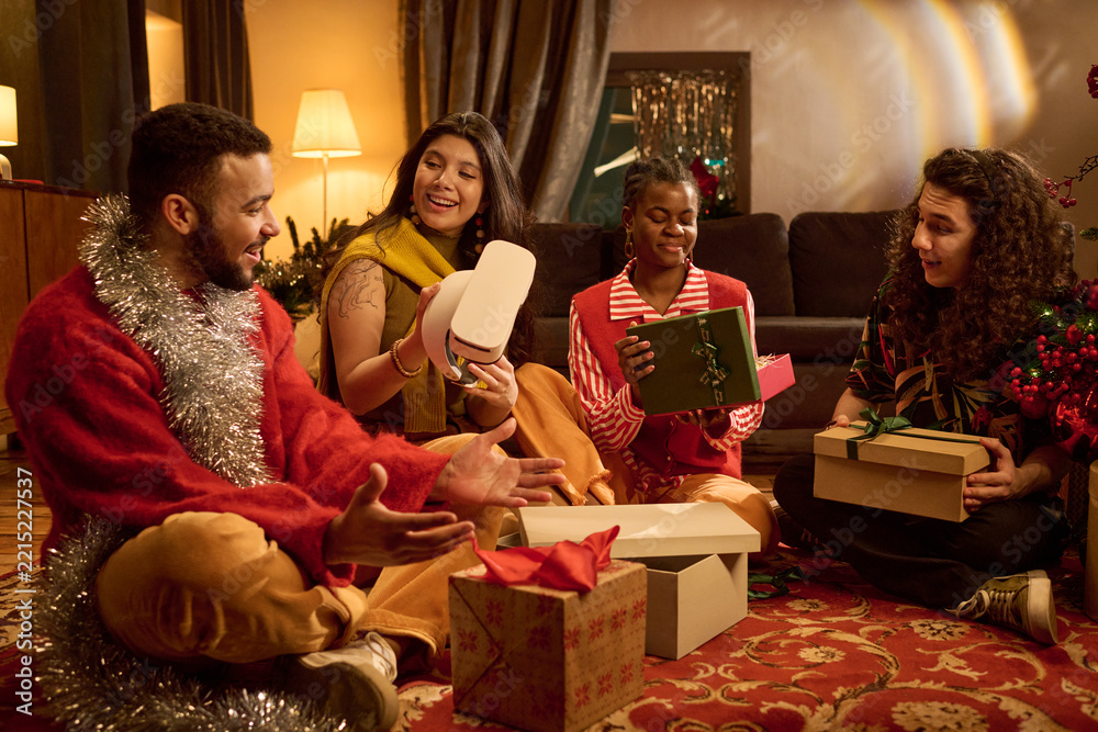 Fototapeta premium Multiethnic group of young adult friends unpacking Christmas presents including VR headset together indoors. Suitable for holiday tech advertising and seasonal gift campaign
