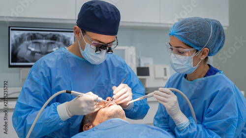 Dental implant procedure with surgeon and assistant working in clinic. Dental surgery includes precision techniques and tools for patient care. Concept dental health and professional medical practice.