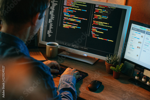 Male developer types code on a computer monitor indoors