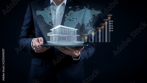 Businessman holding tablet with holographic house model and global real estate data charts