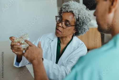 Dentist explains treatment using a tooth model to patient