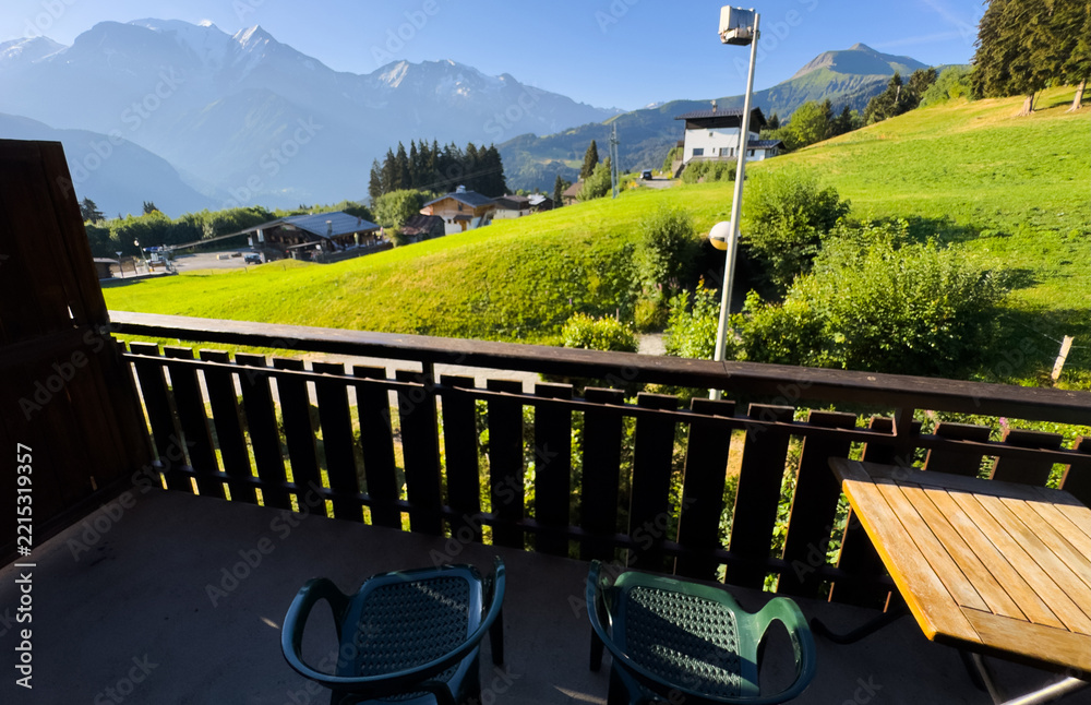 Fototapeta premium cozy wooden balcony with comfortable lounge chair overlooking scenic green mountains