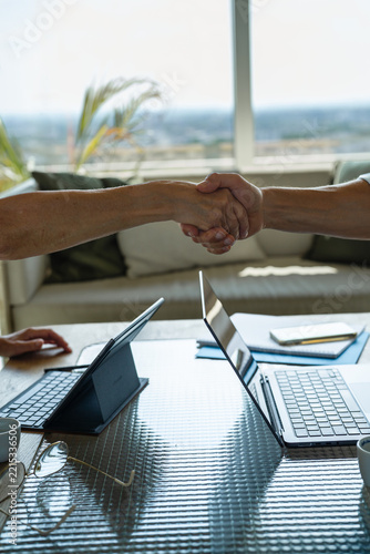 Man and woman shaking hands over a desk during an office meeting