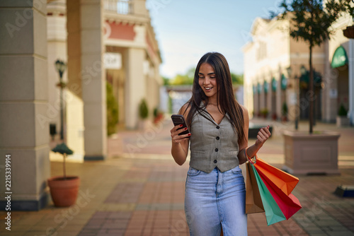 Woman shopping, checking smartphone while holding bags