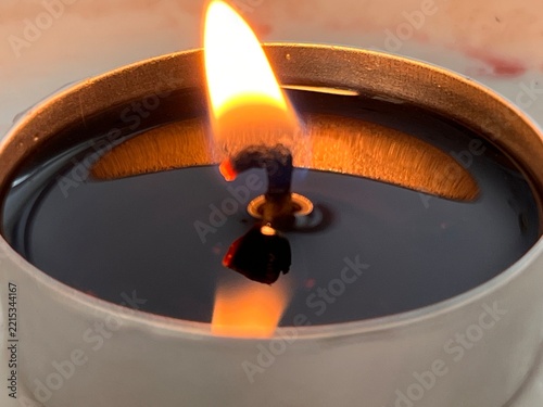 Macro top view of a burning tea light candle with melted wax in a metal cup