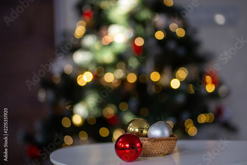 Christmas ornaments in basket with decorated tree and bokeh lights. Christmas ornaments in woven basket with red, gold and silver baubles, decorated Christmas tree with warm bokeh lights