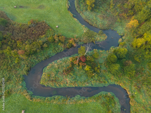 Aerial view of a winding river meander surrounded by autumn meadows and woodland near Bolimów, Poland