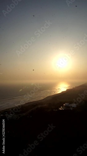 Peaceful sunset landscape showing the silhouette of rolling hills along the seashore with gentle waves under a clear sky.