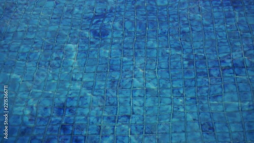 Clear blue swimming pool water texture with ceramic tile pattern visible beneath the calm surface.	