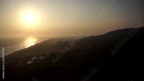 Peaceful sunset landscape showing the silhouette of rolling hills along the seashore with gentle waves under a clear sky.