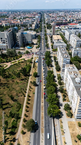 Aerial view of a major urban boulevard with multi-lane traffic, surrounding apartment blocks, and green park areas in Novi Sad, Vojvodina, Serbia.