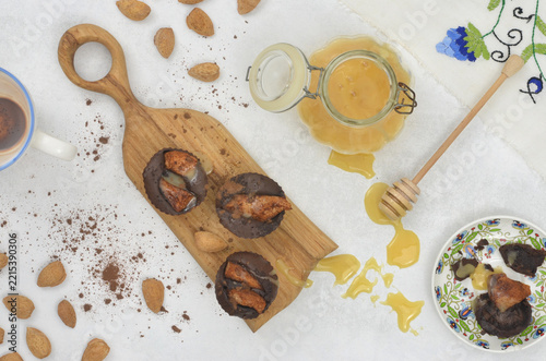 Chocolate muffins with pears on wooden tray. Decorative glass jar with honey and honey stains on the table. A half-eaten cookie,  drunk a chocolate drink in a cup and embroidered tablecloth. 