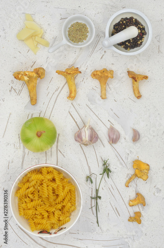 Ingredients for cooking dish with mushrooms: pasta, chanterelle mushrooms, onion, yellow cheese, garlic, pepper and herbs. Everything is arranged in neat rows.