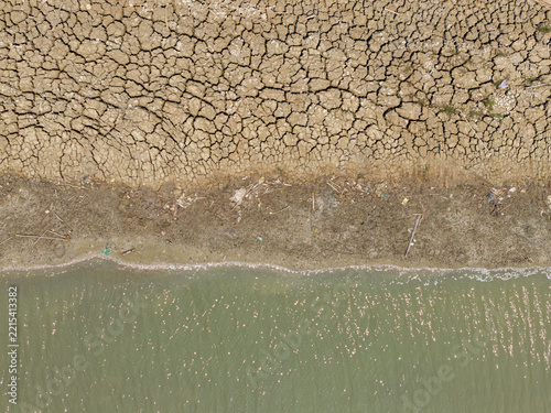 Aerial view of a shrinking river with dry, cracked mud banks and scattered debris during the dry season in Kedung, Central Java, Indonesia.