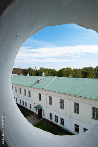 A circular opening frames a view of a church with golden domes in the distance, partially hidden by trees and under a blue sky. The scene shows a mix of nature and architecture.