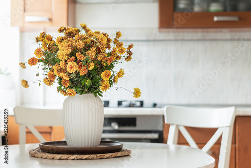 Bouquet of orange chrysanthemums decorates a bright kitchen table, adding natural seasonal color to a modern home interior.