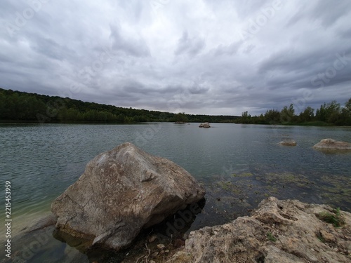 Calm Lake With Rocks Under Dramatic Overcast Sky Surrounded by Forested Shoreline and Moody Light in the Seine-et-Marne