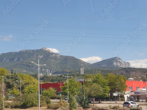 French Alps in Savoie Mountain Landscape With Red Industrial Building, Trees and Urban Road Under Clear Blue Sky
