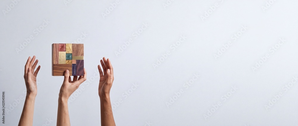 Fototapeta premium Close up of human hands holding a handcrafted square wooden mosaic tile with metallic accents and colorful resin inserts against a clean white background with ample negative space on the right