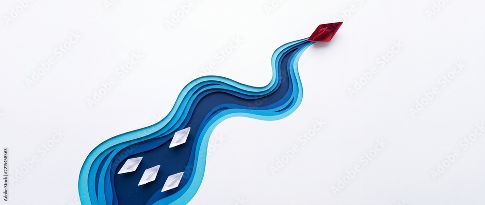 Fototapeta premium Red paper boat leading a group of white paper boats along a winding blue layered paper cut river, conceptual illustration of leadership, business success, individuality, and strategic vision.