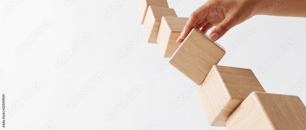 Fototapeta premium A business person's hand arranging wooden cubes in a diagonal line against a white background, representing growth, strategy, building a foundation, and a perspective shift in development.
