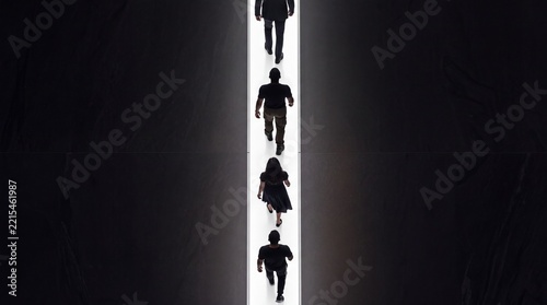 Top down overhead view of diverse people walking in a single file line along a bright glowing path in a dark minimalist space, representing direction, progress, and conceptual leadership.