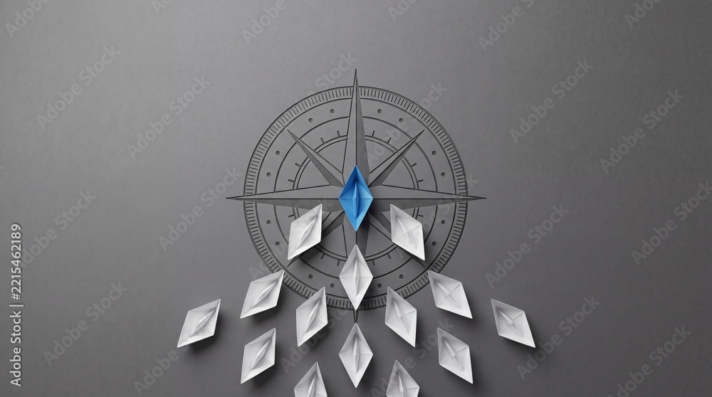 Fototapeta premium Top view of a blue origami paper boat leading white boats towards a compass symbol on a gray background, representing leadership, business strategy, navigation, and professional guidance.