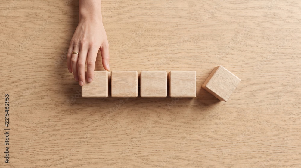 Fototapeta premium Overhead view of a hand arranging a row of blank wooden blocks on a light wooden surface, symbolizing business strategy, planning, organization, structure, and professional growth concepts.