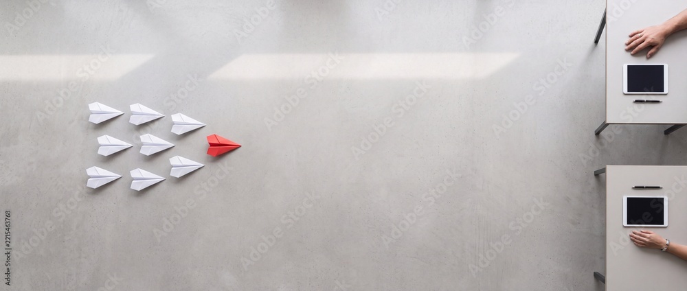 Fototapeta premium Minimalist Wide Flat Lay of a Red Origami Plane Leading White Planes Toward Business Desks with Digital Tablets, Symbolizing Leadership, Strategic Innovation, and Successful Teamwork.