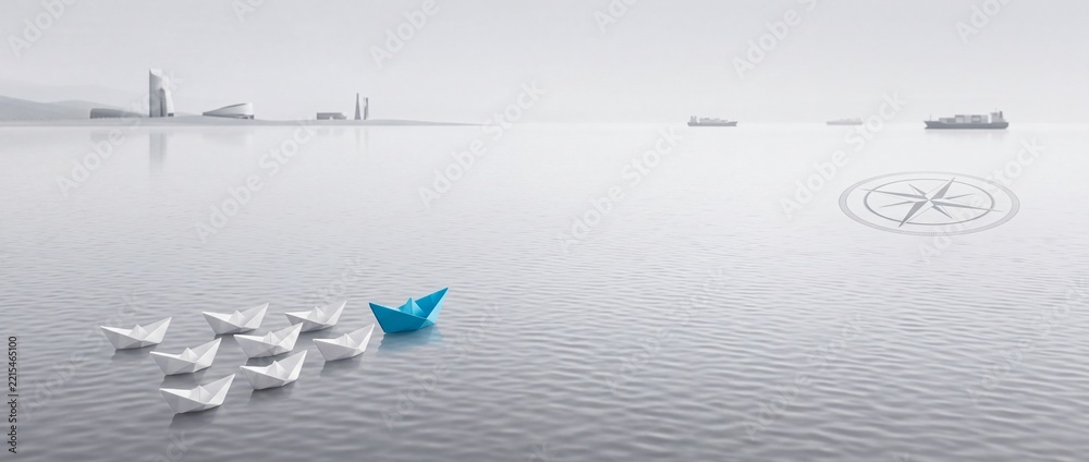 Fototapeta premium Leadership and business strategy concept featuring a blue paper boat leading white origami boats on calm water with industrial cargo ships and a navigation compass icon in wide context.