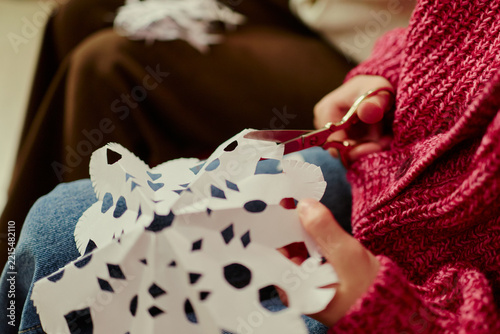Close up of Caucasian child hands cutting paper snowflake with scissors during winter craft activity. Image suitable for holiday art workshop marketing or creative education campaigns