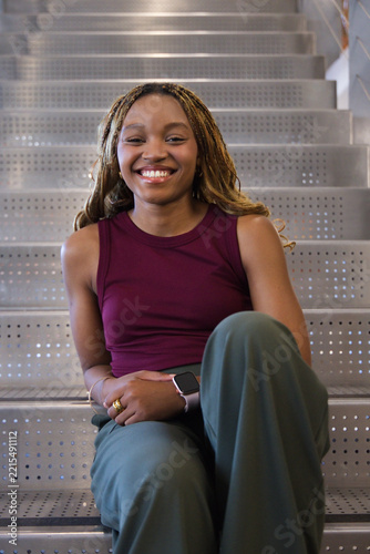 Adult African American woman sitting on perforated steps wearing maroon top, smartwatch with rings