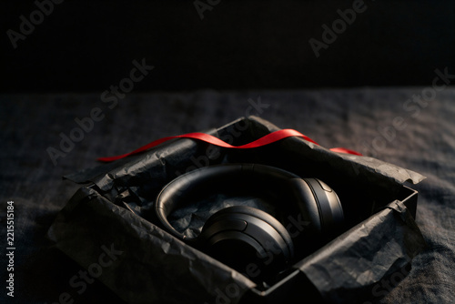 Black headphones in open gift box with red ribbon and black tissue