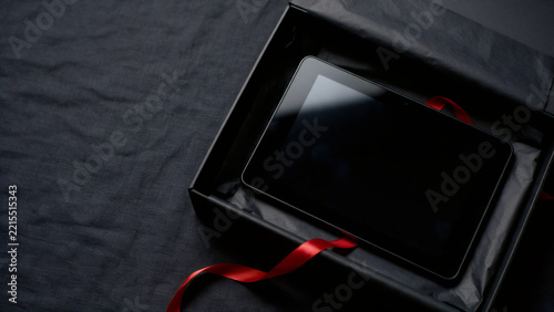 Tablet with powered off screen in open black gift box with red ribbon