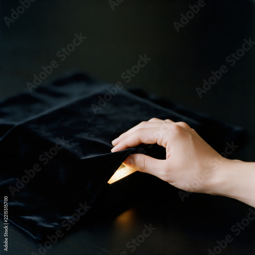 Hand lifting black velvet cloth to reveal glowing golden light