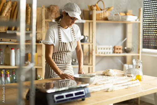 Female baker prepares raw yeast dough in bakery, forming it into long sausages to be cut into pieces for baking buns