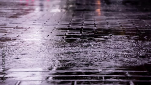 Rainy Day in the City. Drops of rain fall on the paving slab. On a wet surface, the lights of the city are reflected