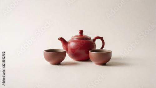 Red ceramic teapot with two brown tea cups on light background