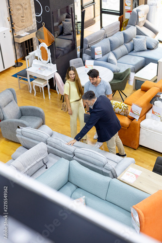 Salesman showing sofa to young couple in furniture store