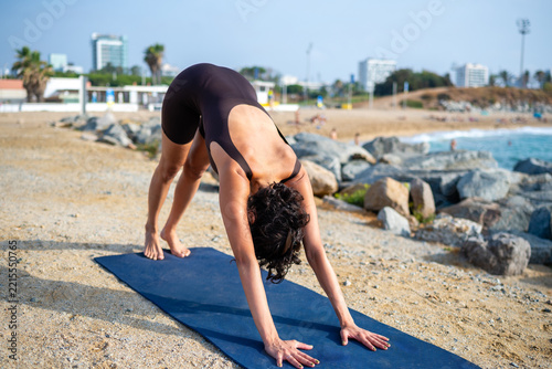 Woman practicing downward dog yoga pose on beach