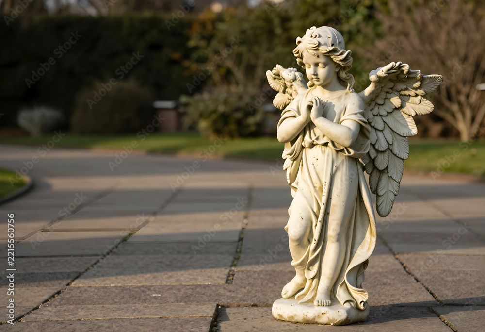 Fototapeta premium Spirituality and mourning, stone angel statue with hands in prayer standing on a cemetery path for funeral remembrance and religious peace in a garden