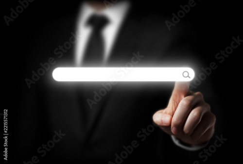 Businessman finger touching glowing white search bar with magnifying icon on black background, internet search concept.